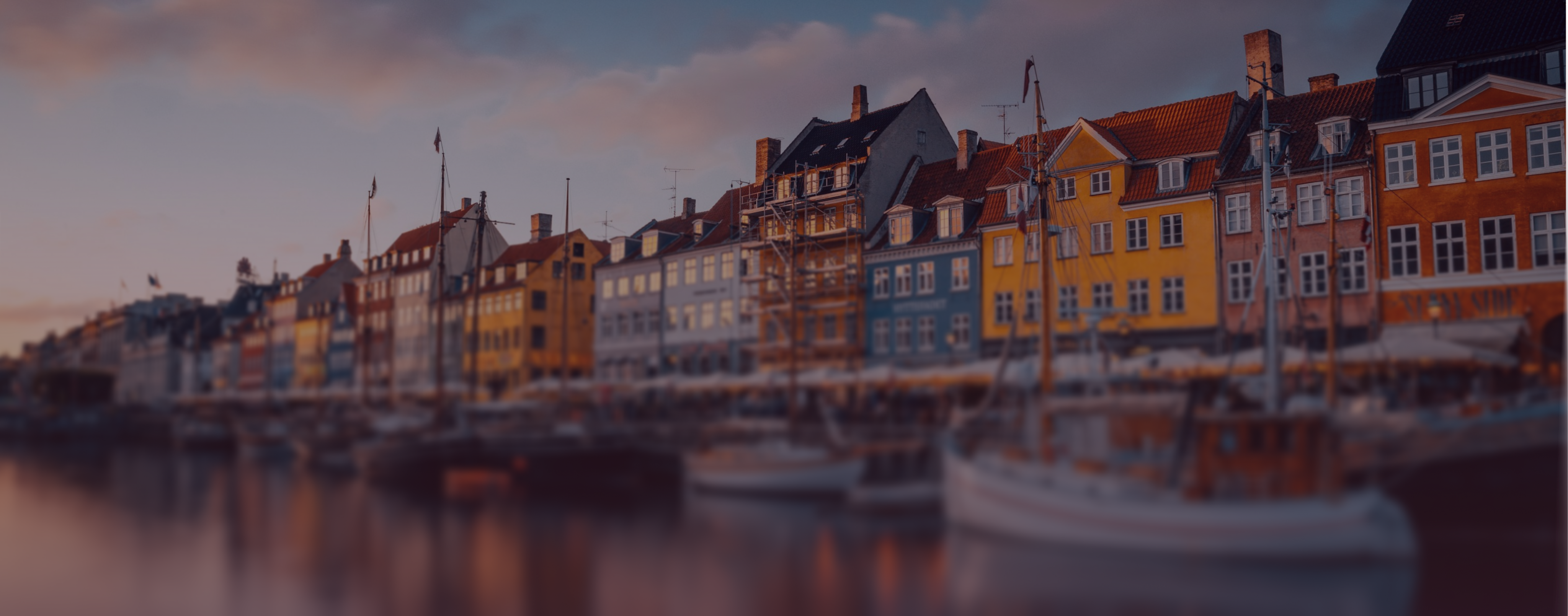 Colorful historic buildings and docked boats along Copenhagen's waterfront at dusk.