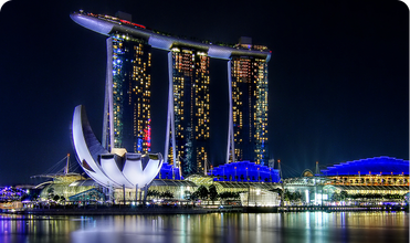 Marina Bay Sands and the lotus-shaped ArtScience Museum illuminated at night, with colorful lights reflecting across Singapore’s waterfront.